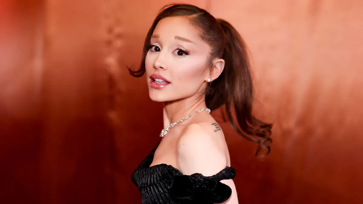 Ariana Grande performing on stage, singing into a microphone with bright lights in the background.