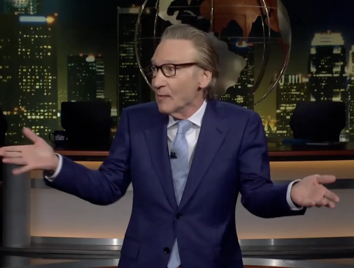 Bill Maher on stage looking at the audience with an uncomfortable expression on 'Real Time'.