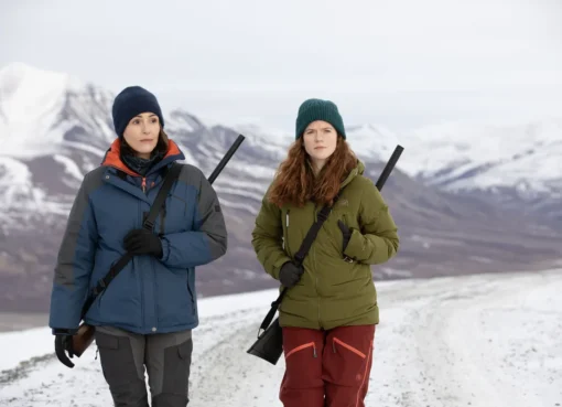Suranne Jones and Rose Leslie in winter gear, trekking across a snowy Arctic landscape with rifles.