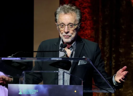 Frankie Valli smiling and singing into a microphone on stage.