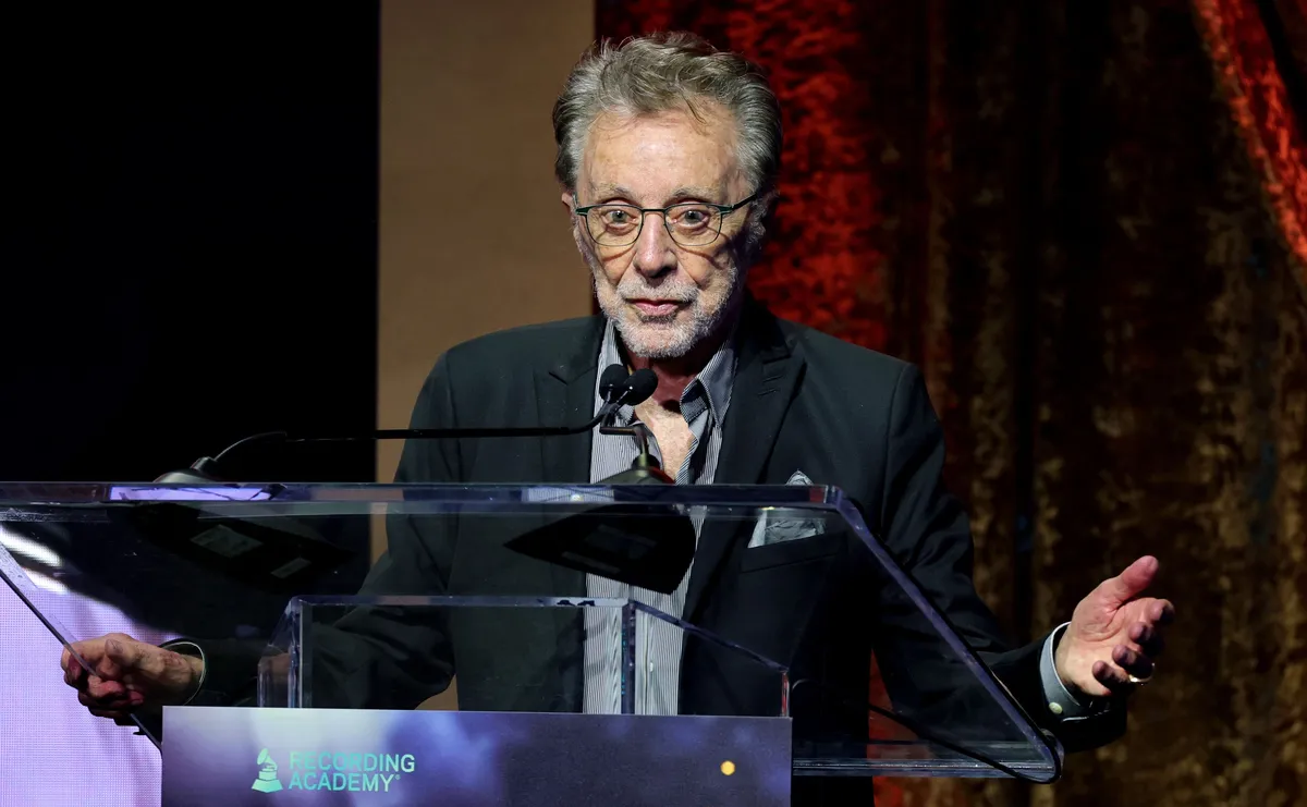 Frankie Valli smiling and singing into a microphone on stage.