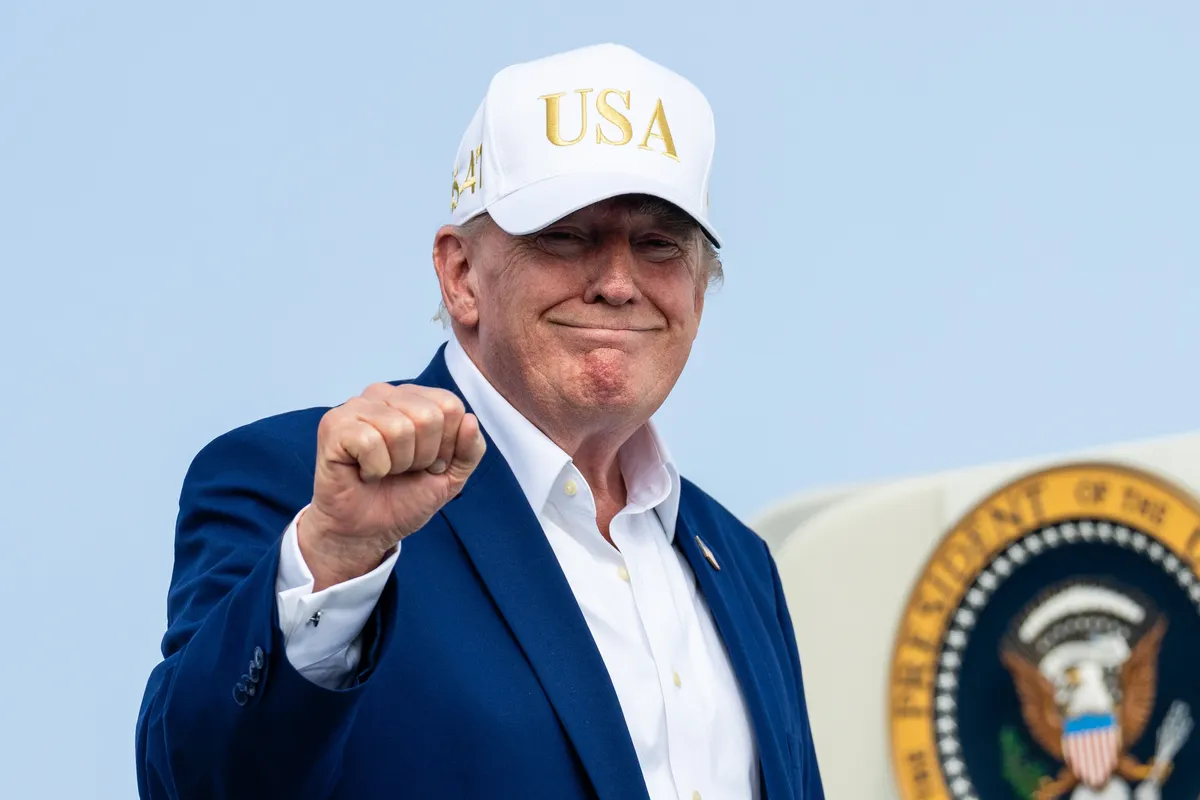 President Donald Trump speaking at a podium, possibly with a subtle film or Hollywood backdrop.