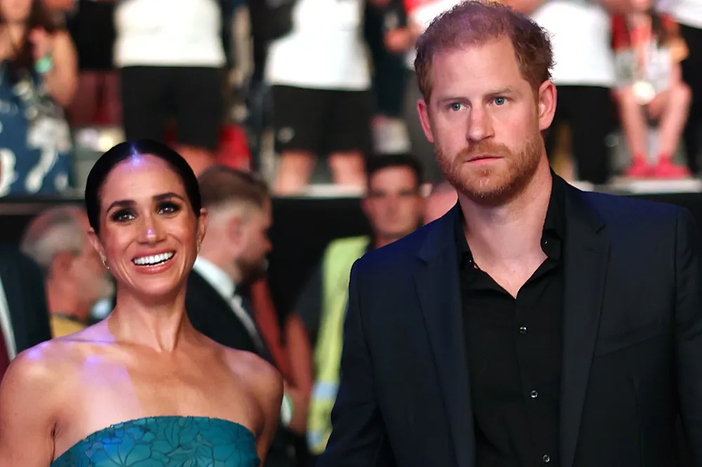 Prince Harry and Meghan Markle smiling and waving at an event.