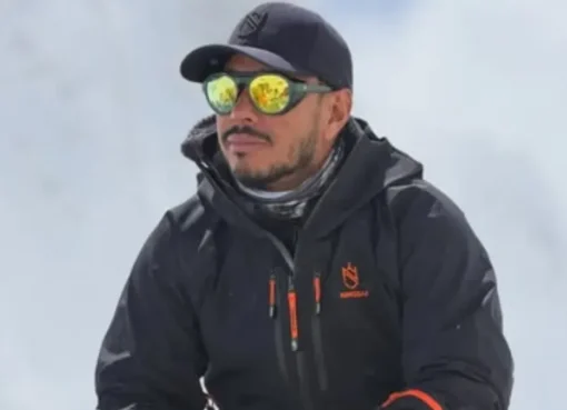 Portrait of Nepalese mountaineer Nirmal Purja, Nimsdai, smiling against a snowy mountain background.