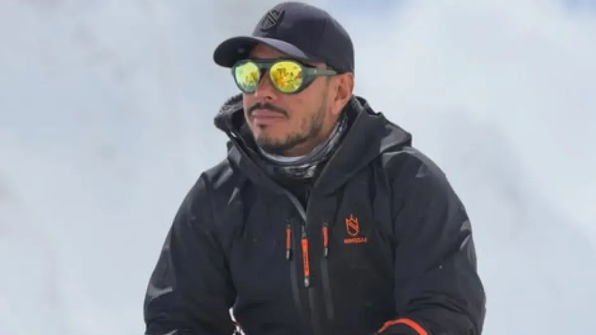 Portrait of Nepalese mountaineer Nirmal Purja, Nimsdai, smiling against a snowy mountain background.