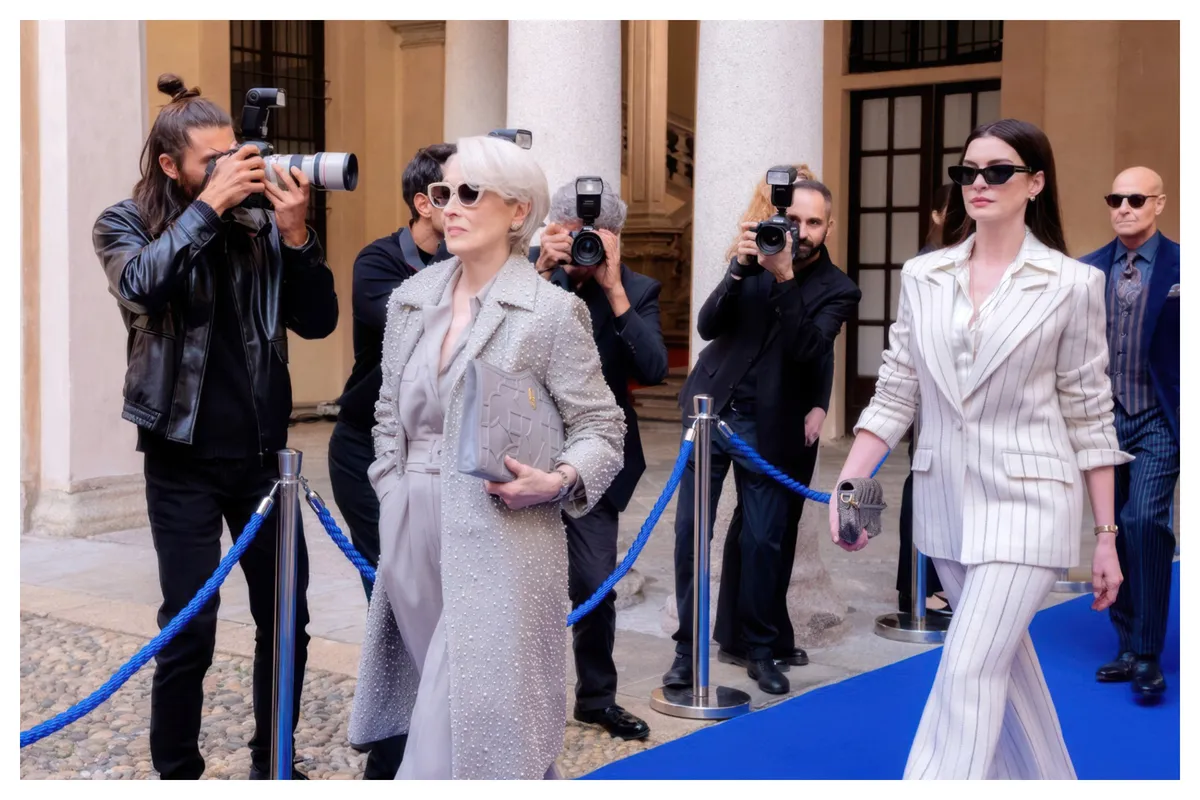 A stylish woman in a chic outfit walking confidently down a historic street in Milan, possibly near a film location from 'The Devil Wears Prada 2'.