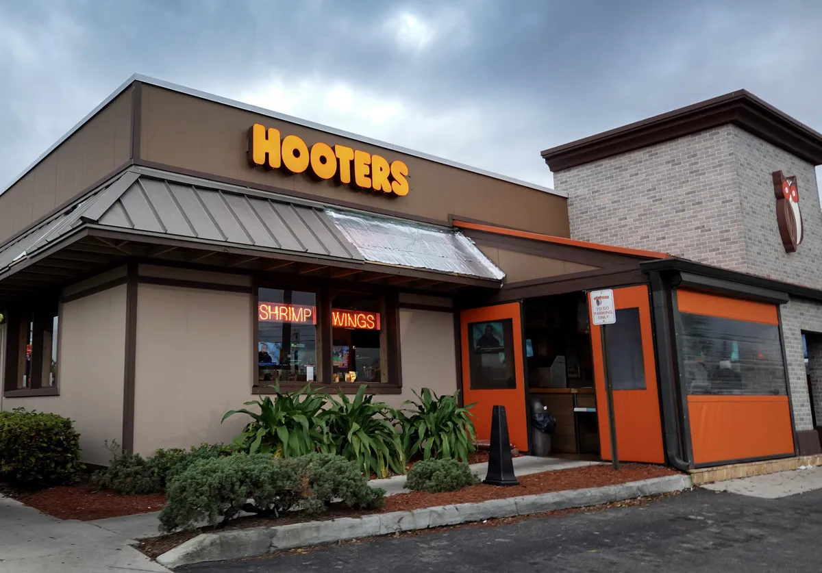 A film clapperboard over a Hooters logo with a beach background.