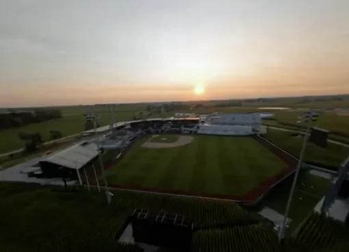 A baseball field at dusk with a farmhouse in the background.
