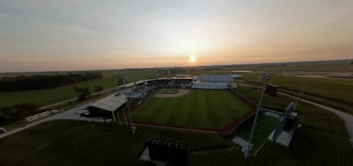 A baseball field at dusk with a farmhouse in the background.