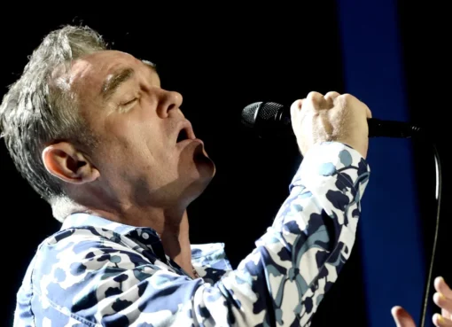 Morrissey performing on stage with a spotlight on him, singing into a microphone.