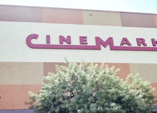 Three movie theater marquees, representing AMC, Regal, and Cinemark, lit up against a night sky.