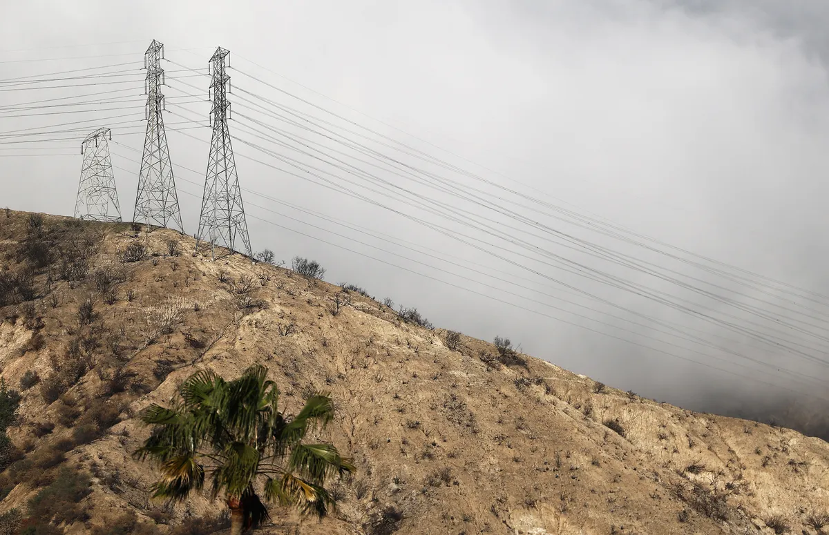Photo of a burned transmission tower with smoke in the background.