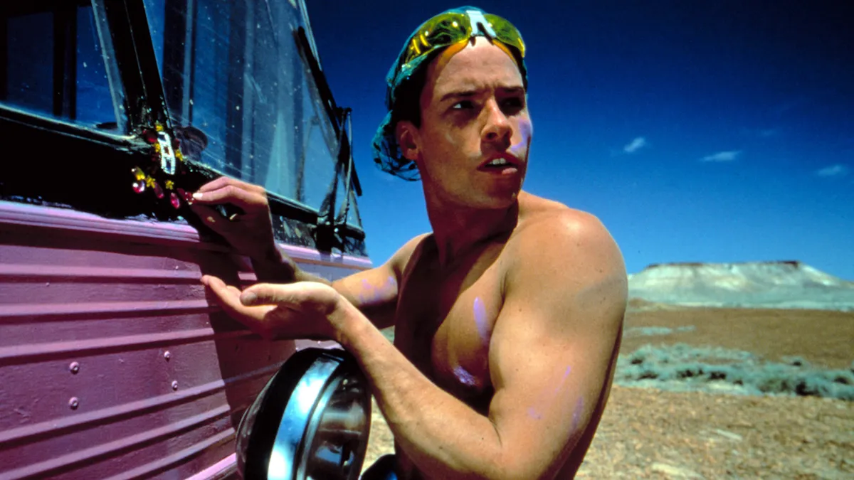 Guy Pearce in a bright, colorful costume from Priscilla, Queen of the Desert, standing in the Australian Outback.