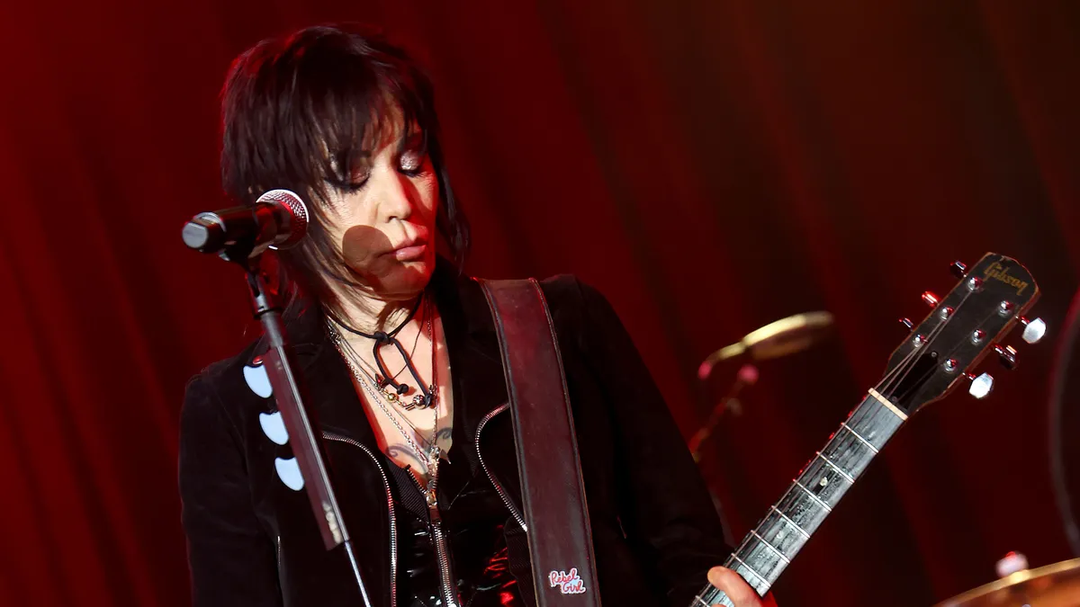 Joan Jett on stage, holding a guitar, under bright lights.