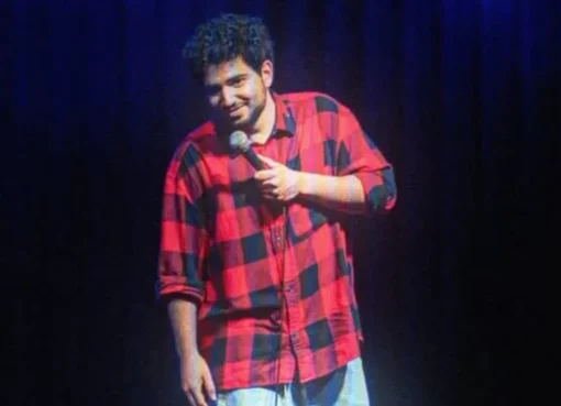 Comedian Samay Raina performing stand-up comedy on a dark stage