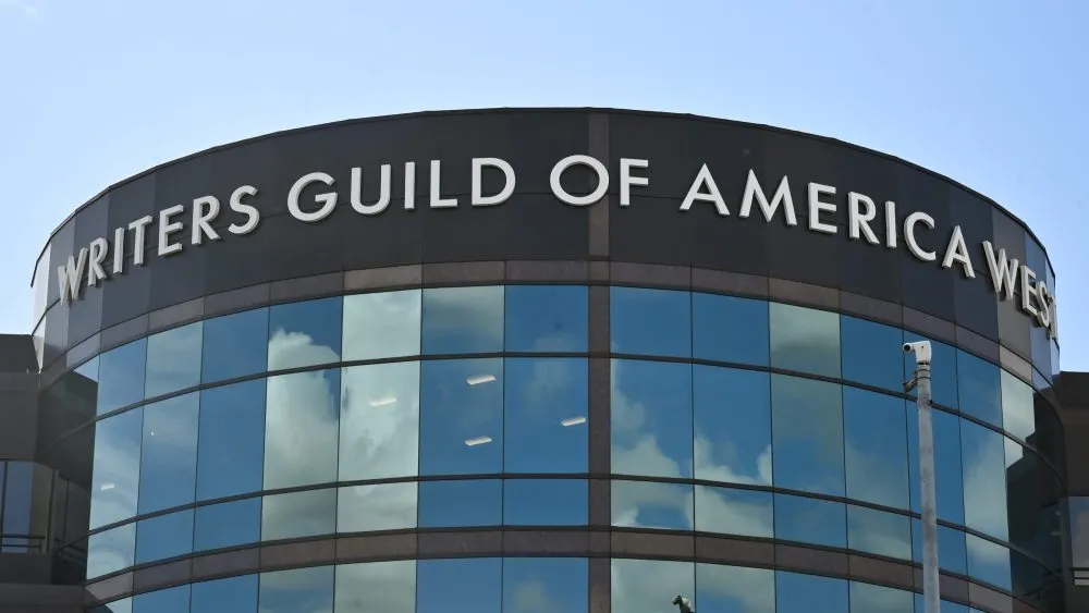 A dramatic image showing a studio building being packed up, with a stern-looking WGA logo overlaid.