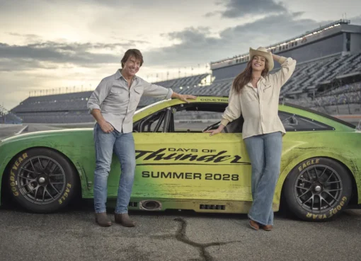 Anne Hathaway and Tom Cruise standing with a sleek race car.