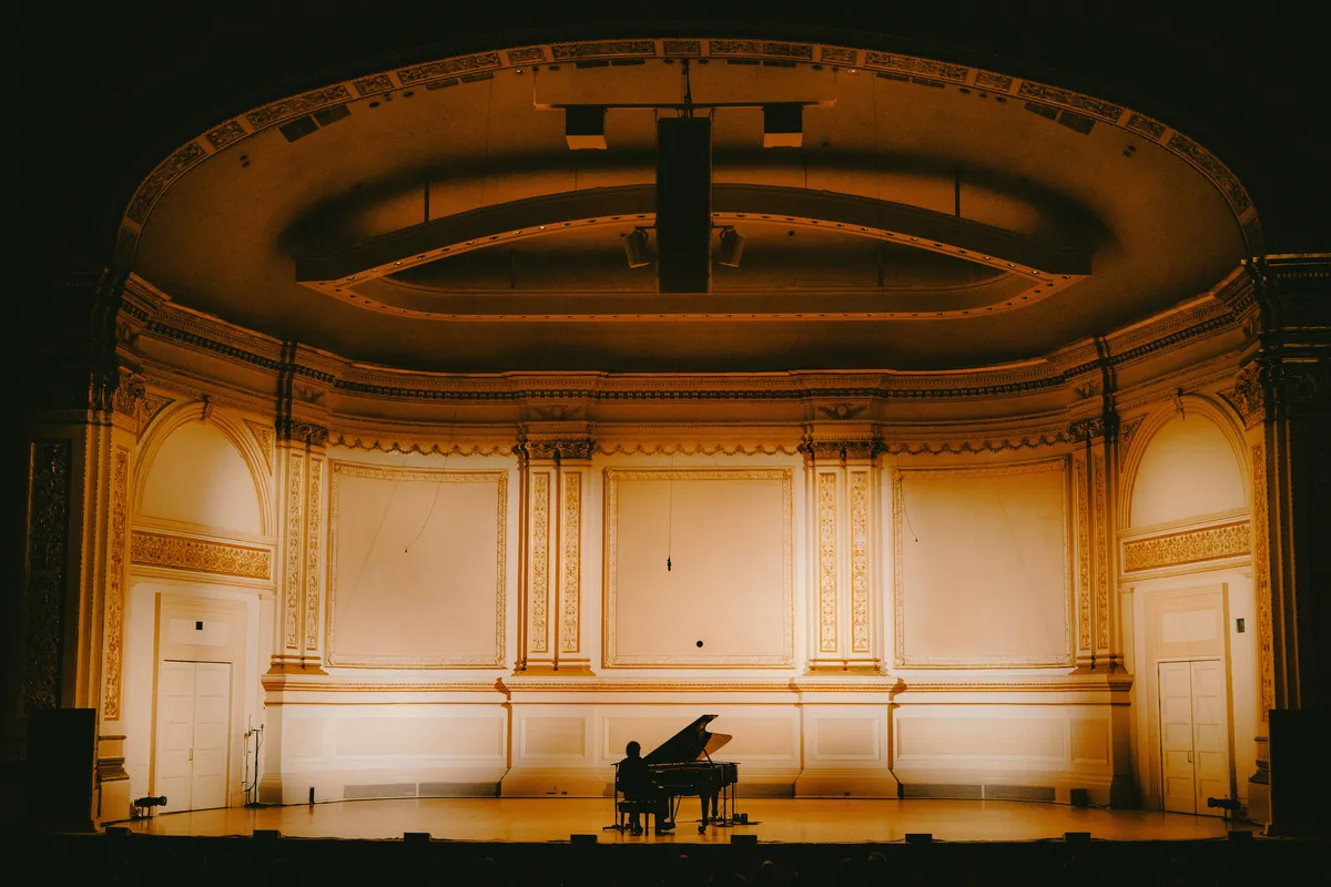 Paul Thomas Anderson and Cameron Winter on stage at Carnegie Hall, bathed in warm stage lights.