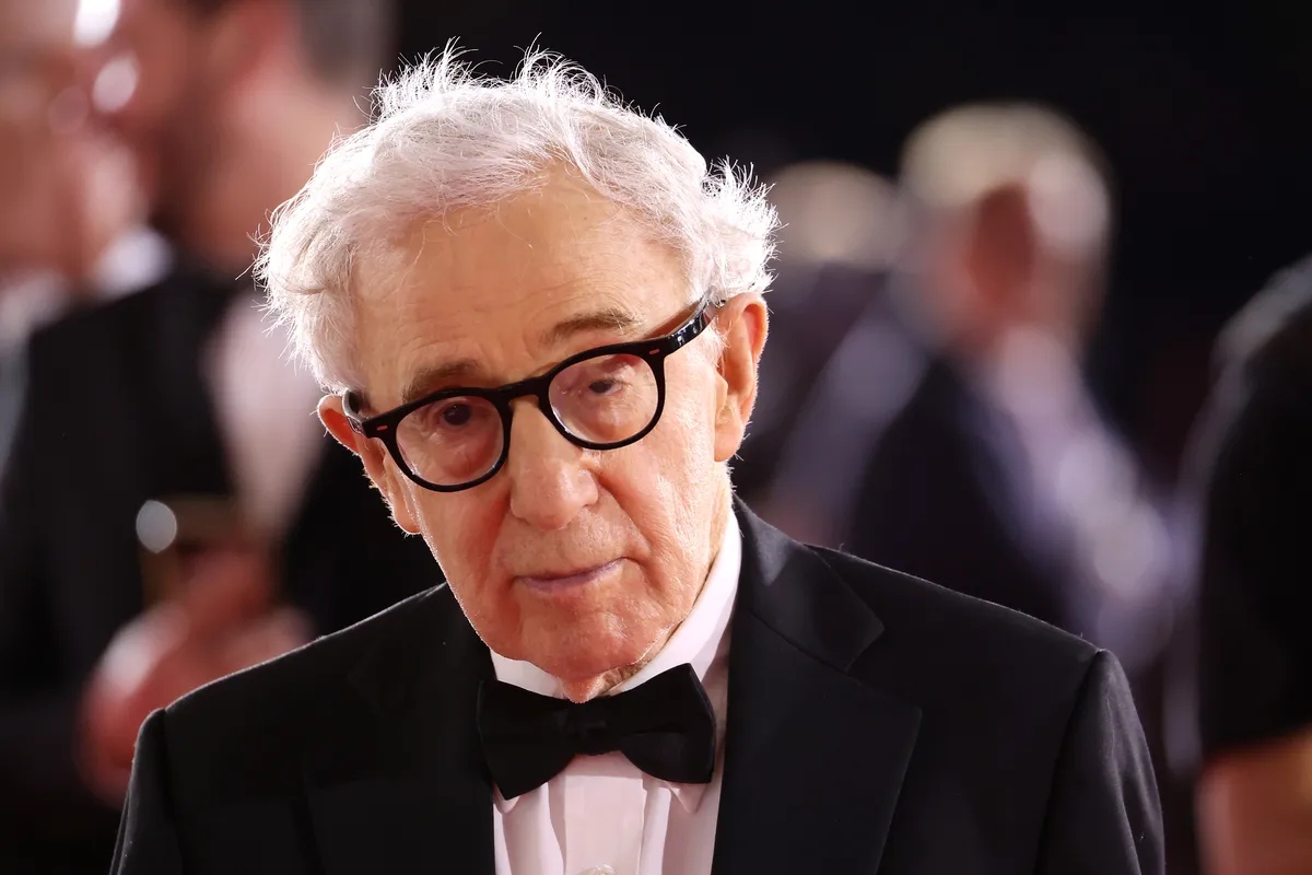 Woody Allen smiling, with a subtle backdrop hinting at a Spanish street scene.