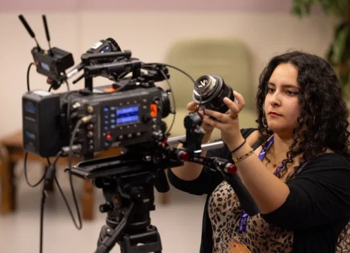 A diverse group of young adults, aged 16-25, enthusiastically collaborating on a film set, with cameras, lights, and crew equipment visible, suggesting hands-on learning.