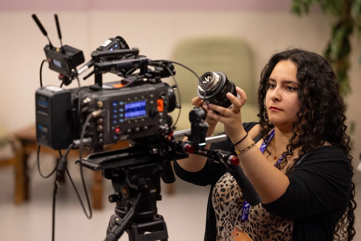 A diverse group of young adults, aged 16-25, enthusiastically collaborating on a film set, with cameras, lights, and crew equipment visible, suggesting hands-on learning.