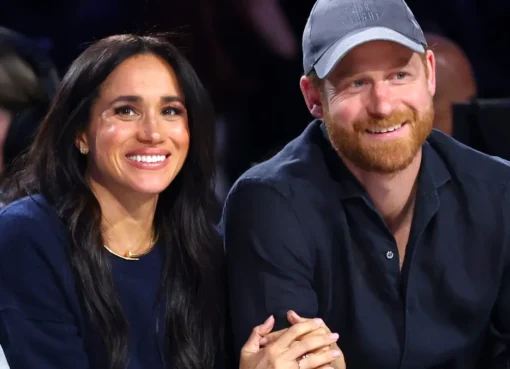 Prince Harry and Meghan Markle smiling and waving to a crowd.