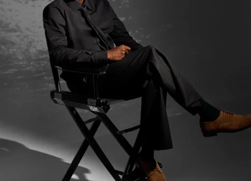 Chris Rock looking thoughtful, possibly on a film set, with a slight smile.
