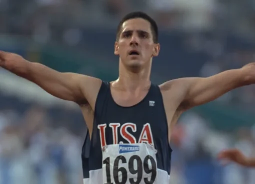 Close-up of a smiling Tony Volpentest, a Paralympic athlete, with a blurred track in the background.