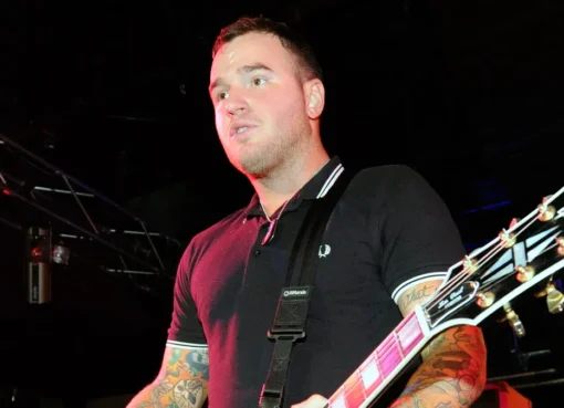 Chad Gilbert, guitarist for New Found Glory, smiling and playing his guitar on stage.