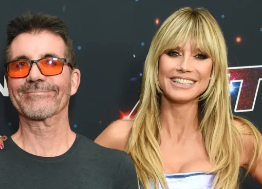Heidi Klum smiling at a judging table with bright lights in the background