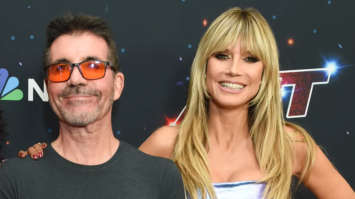 Heidi Klum smiling at a judging table with bright lights in the background