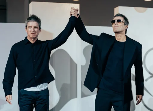 Liam and Noel Gallagher standing side-by-side, raising clasped hands triumphantly at the Venice Film Festival premiere.