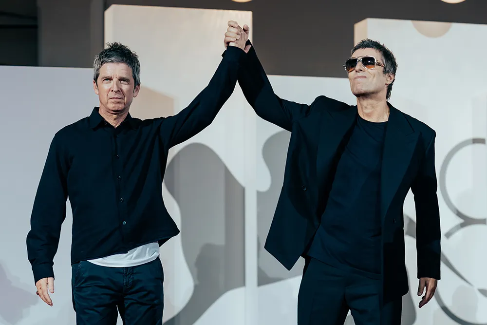 Liam and Noel Gallagher standing side-by-side, raising clasped hands triumphantly at the Venice Film Festival premiere.