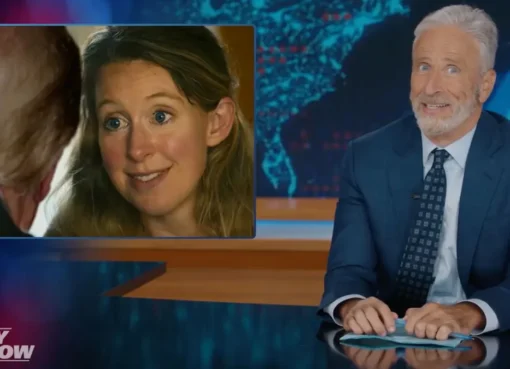 Jon Stewart sitting at his desk on The Daily Show set