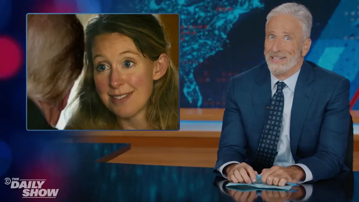 Jon Stewart sitting at his desk on The Daily Show set