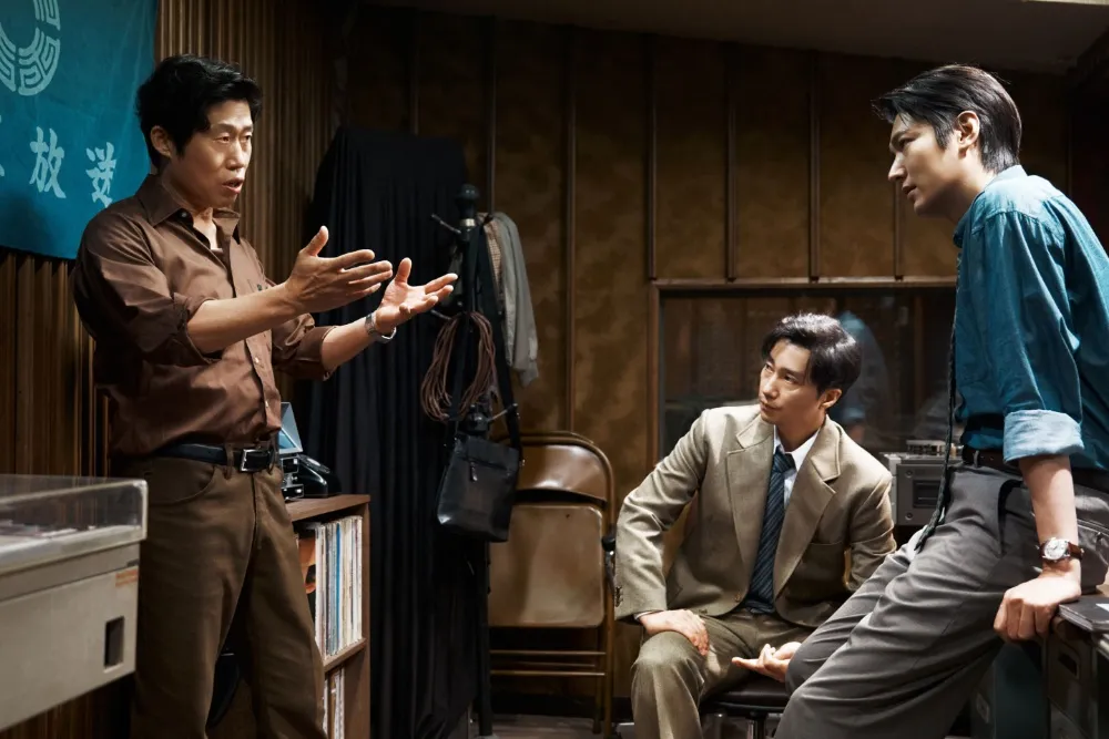A movie poster for 'The Assassin(s)' featuring a serious-looking character, with text in Korean and English, hinting at a political crime thriller.