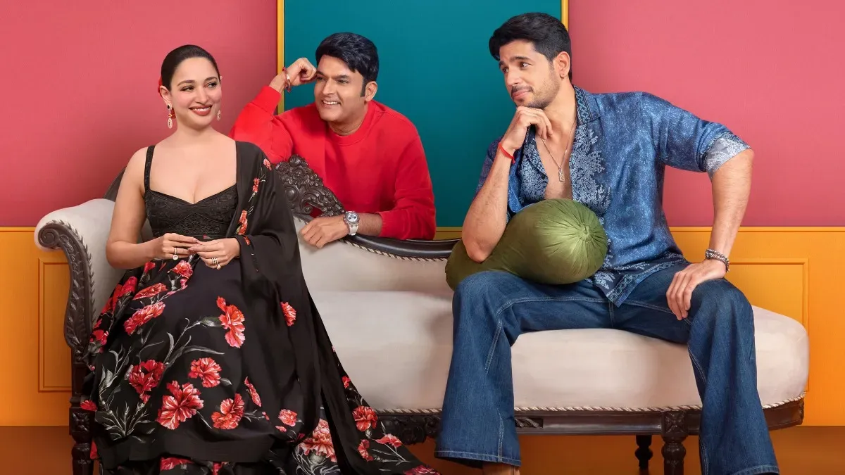 Kapil Sharma laughing with Sidharth Malhotra and Tamannaah Bhatia on his show stage, with bright lights.