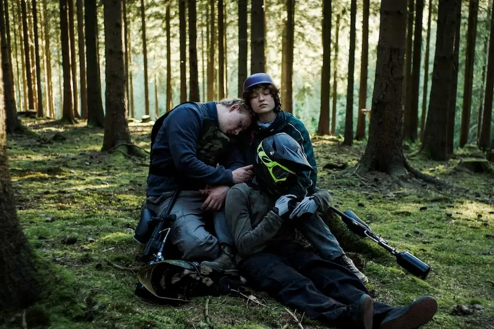 Three teenagers walking into a dark, dense forest.