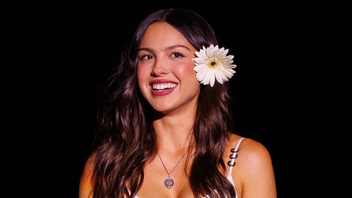Olivia Rodrigo smiling on stage at a festival.