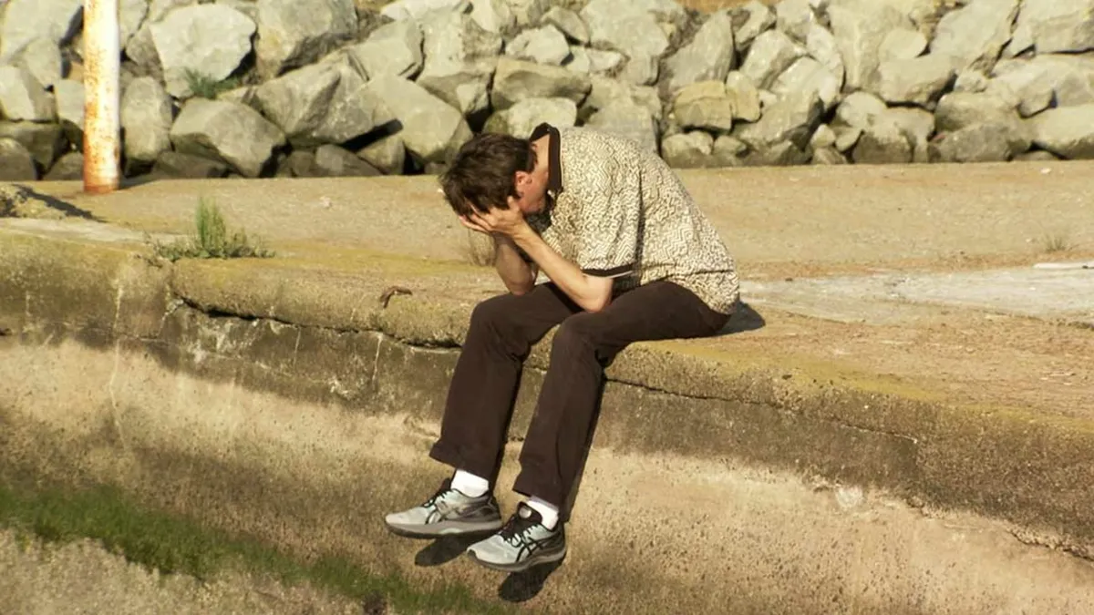 A comedian looking thoughtfully at old video footage, perhaps from a camcorder screen.