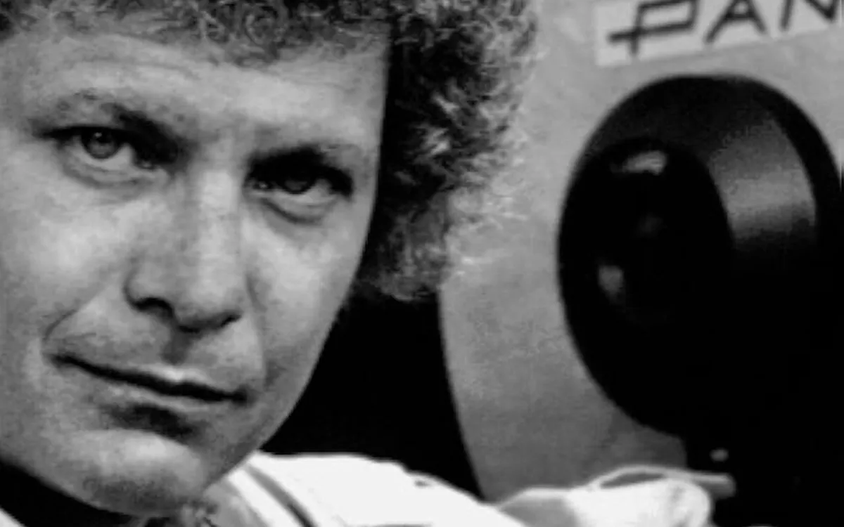 A black and white photo of a smiling David Worth holding a film camera on a movie set.