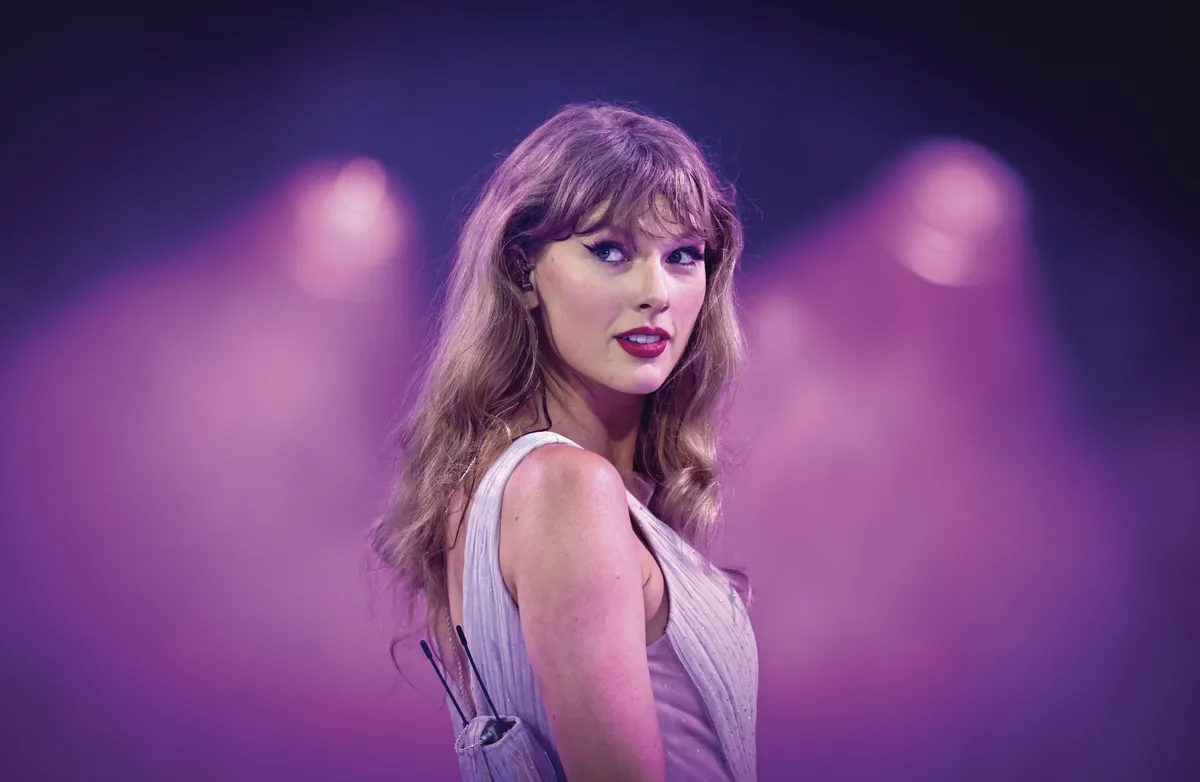 Taylor Swift performing on stage with a microphone, bathed in dramatic stage lighting.