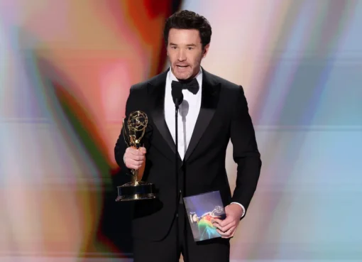 Tom Pelphrey holding his Emmy award on stage.