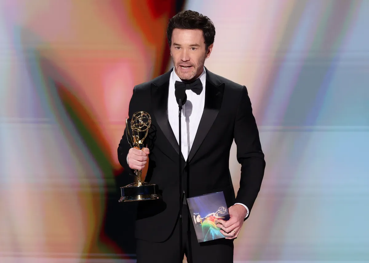Tom Pelphrey holding his Emmy award on stage.