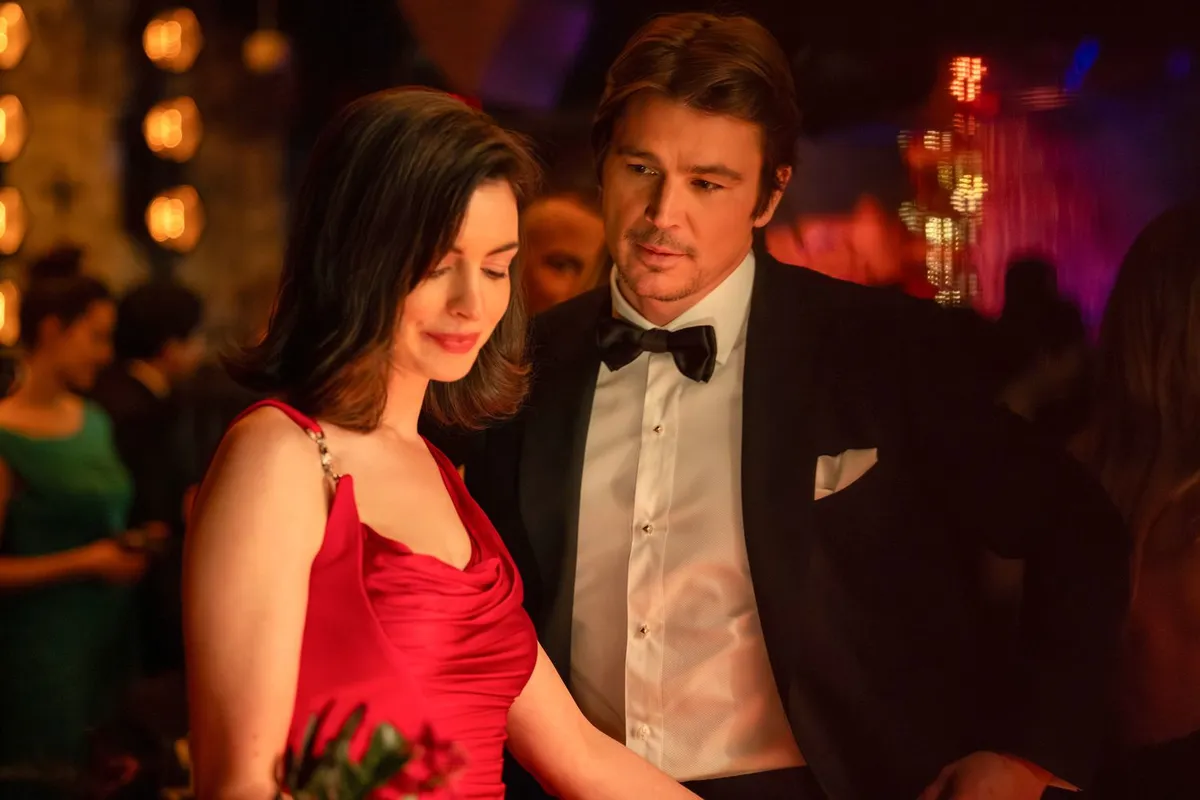 Dakota Johnson and Anne Hathaway looking serious in a dimly lit scene from the movie 'Verity'.