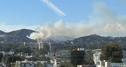 Smoke rising from hills near a large building.