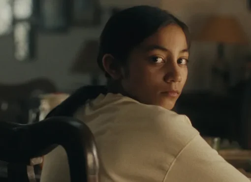 A young girl with a serious expression, likely from the film 'Our Share of Sand', set against an Indian backdrop.