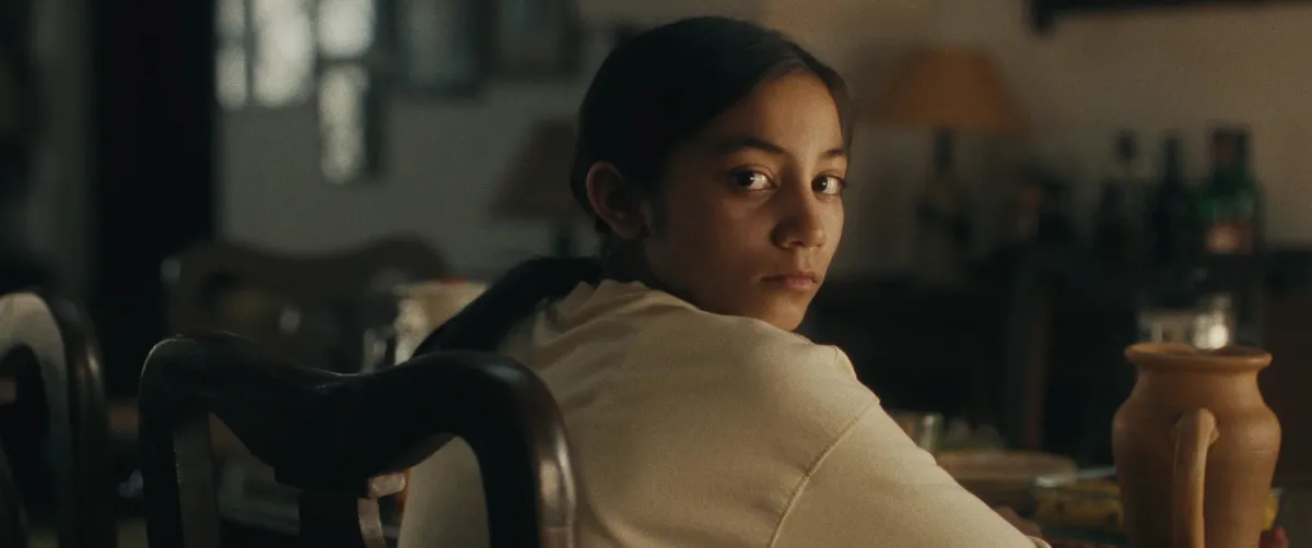 A young girl with a serious expression, likely from the film 'Our Share of Sand', set against an Indian backdrop.