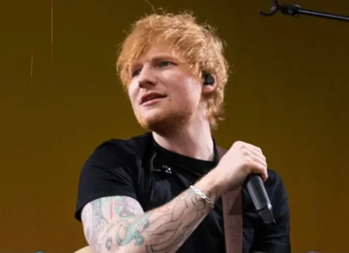 Ed Sheeran on stage with a guitar, a spotlight shining on him, at a concert.