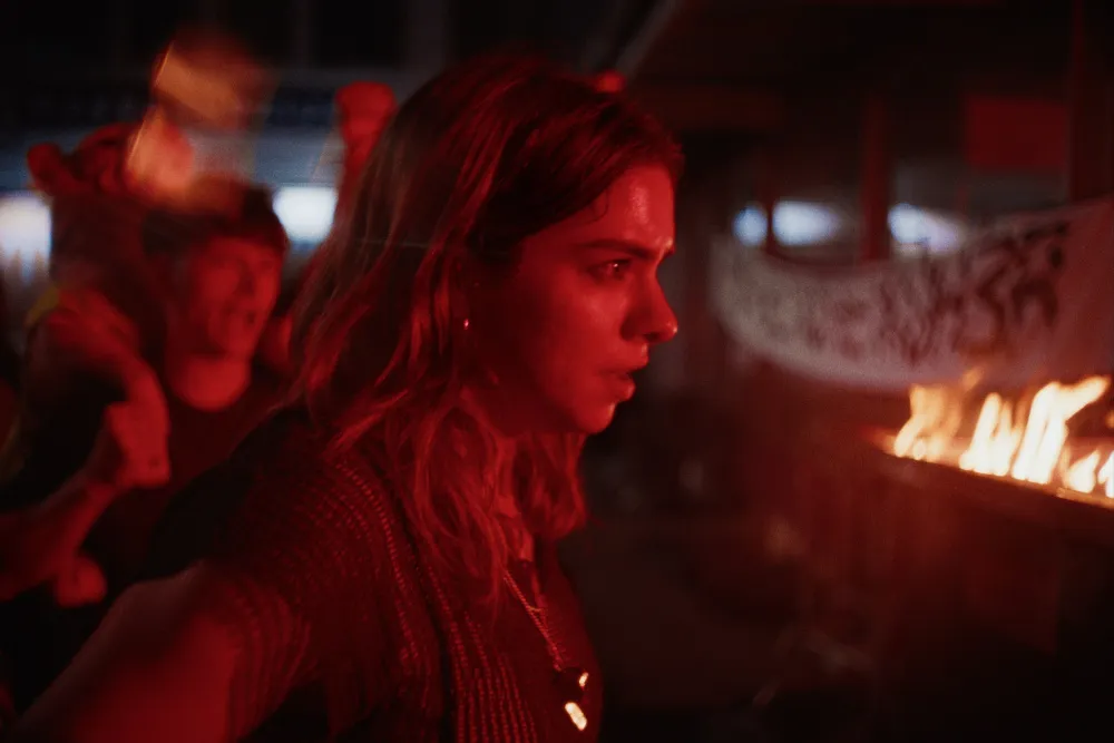 Two young people, one looking rebellious, amidst a protest backdrop from the film 'Until the Day Ends'.